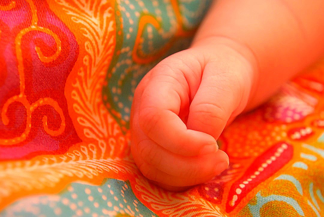 A baby's hand rests on colorful patterned fabric.