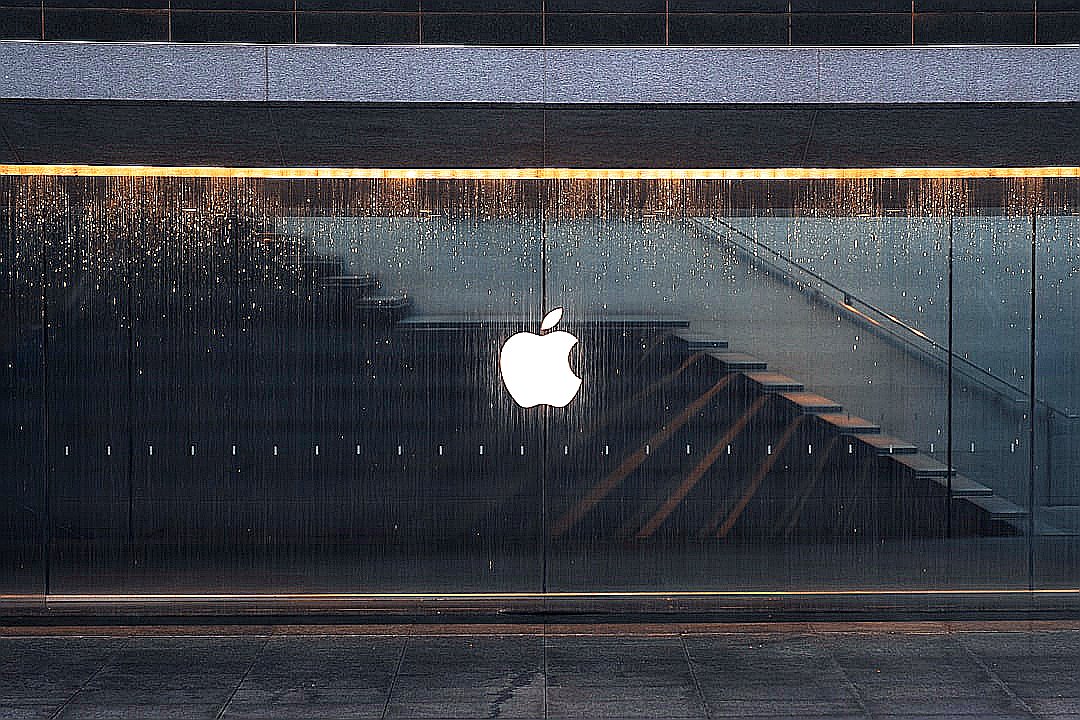 An apple logo is reflected in the glass of a building
