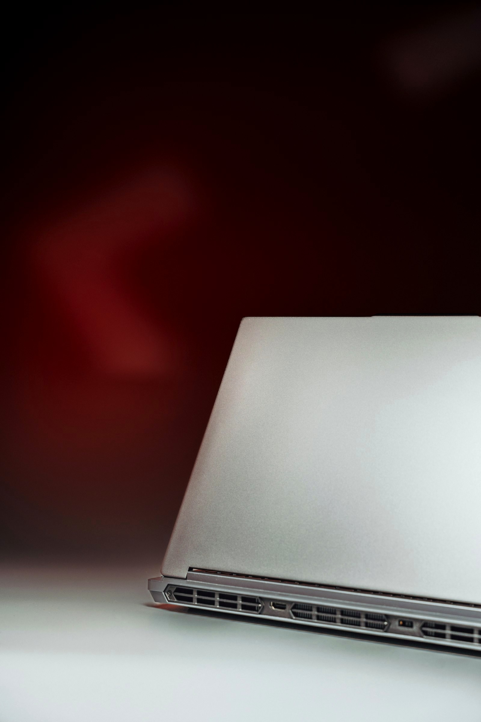 A 3D render of a closed silver laptop against a dark red gradient background